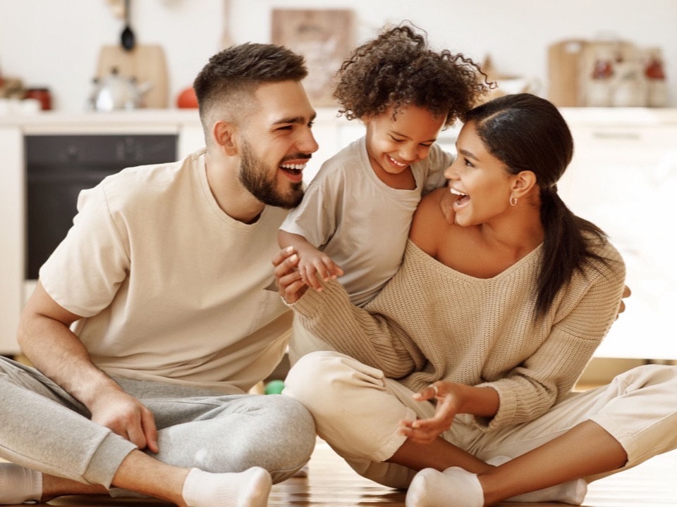 A young family sitting together at home in a bright kitchen — radon testing protects what matters most
