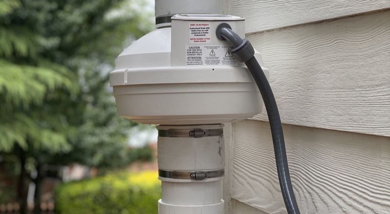 Close-up of an installed radon mitigation fan and exhaust pipe on the exterior of a residential home