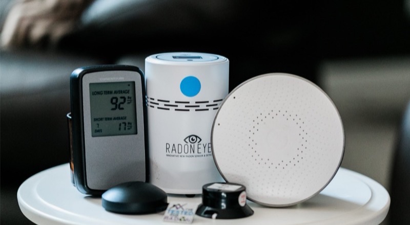 Three professional radon monitoring devices set up on a table — long-term and short-term detectors used in home testing